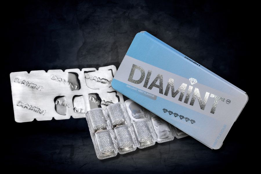 Silbernes Edelsteinobjekt mit synthetischen Diamanten in PVC-Blisterverpackung und digital bedruckter Papierverpackung mit Aufschrift 'DIAMINT', quasi eine Kopie von Kaugummis im Blister.